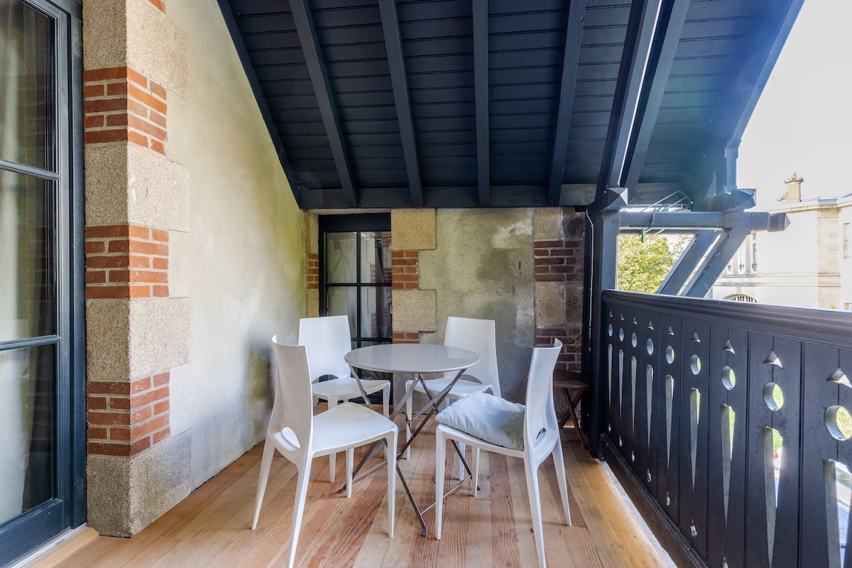 A balcony with a round table and four chairs, a brick wall, and a black railing.