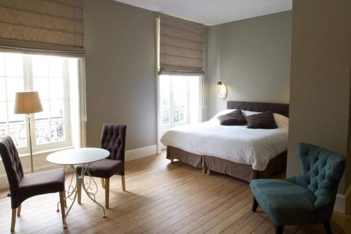 A hotel room with a bed, two chairs, a small table, and a window with blinds.