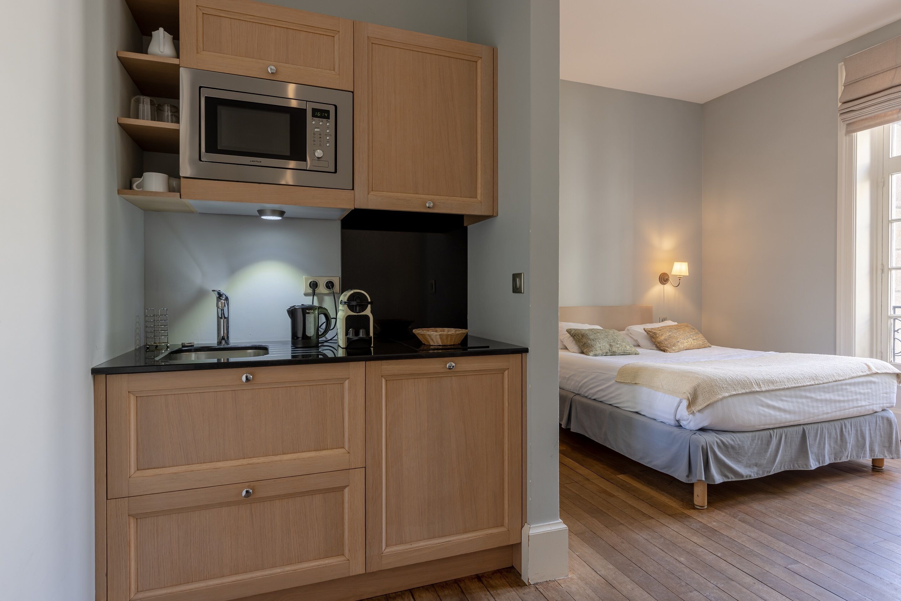 Habitación compacta con cama, mesita de noche y un pequeño rincón de kitchenette que incluye un microondas y una cafetera.