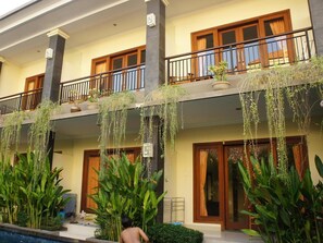 A multi-story building with balconies, large windows, and hanging plants. - Waringin Home Stay (Kuta)