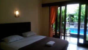 A hotel room with a bed, a nightstand, a window with curtains, and a view of a pool and greenery outside. - Waringin Home Stay (Kuta)