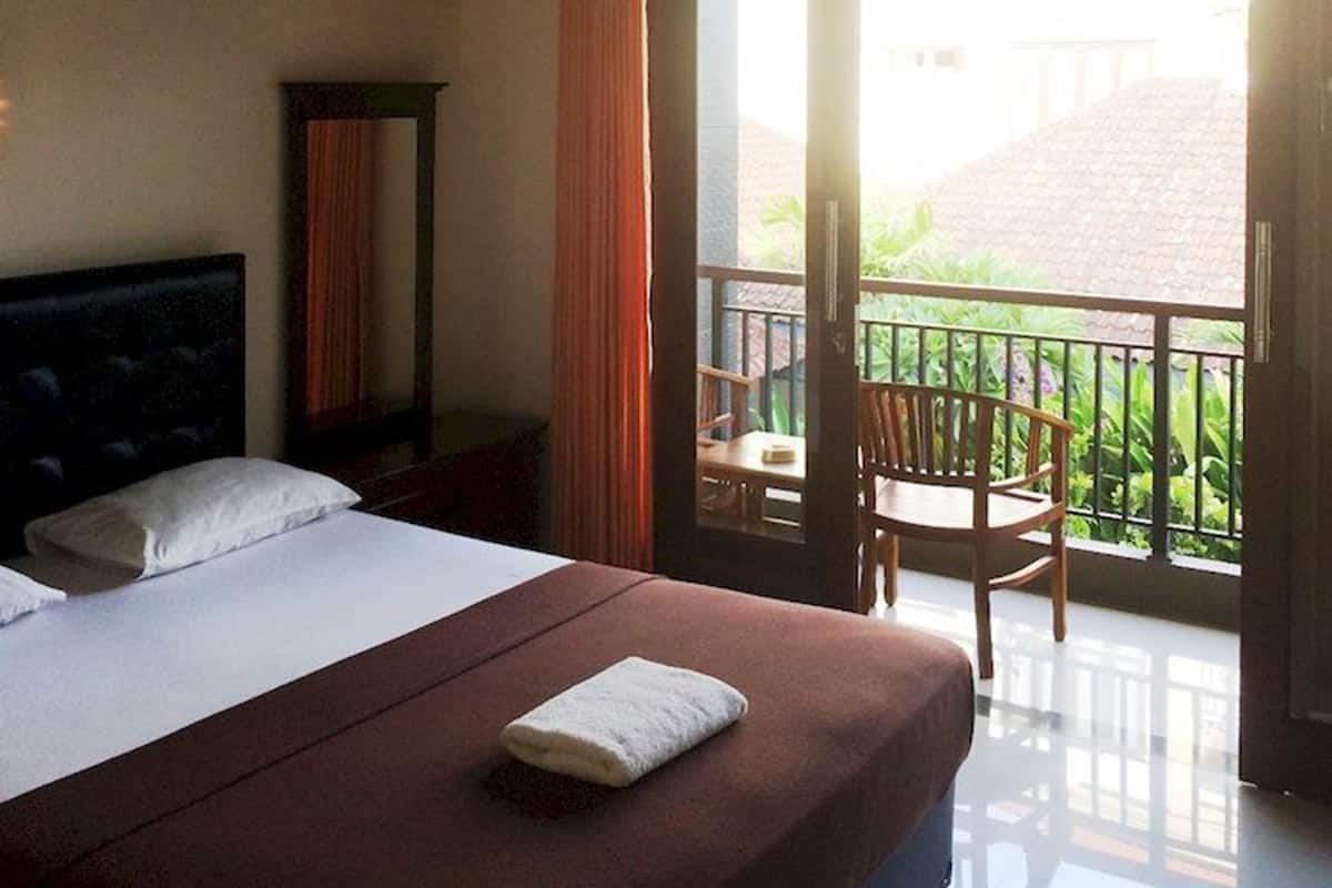 A hotel room with a bed, a nightstand, a ceiling fan, and a balcony with a chair.