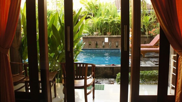 A room with a view of a swimming pool, surrounded by lush greenery and a red chair. - Waringin Home Stay (Kuta)
