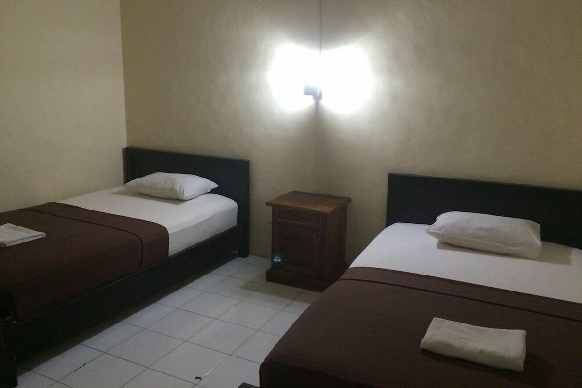 A room with two single beds, a nightstand, and a wall-mounted light fixture.