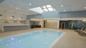 A modern indoor swimming pool with a skylight, a reception area with a bar, and lounge chairs. - Dave Hotel Yerevan (Yerevan)
