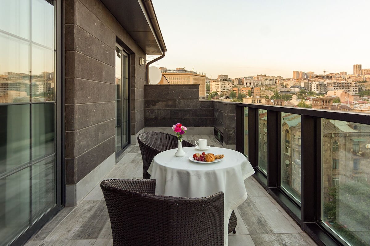 A balcony with a table set for two, a vase of flowers, and a cityscape view.