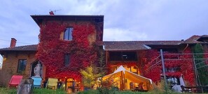 Un edificio rústico con muros cubiertos de hiedra, una pequeña estatua y un área de asientos al aire libre con toldo.