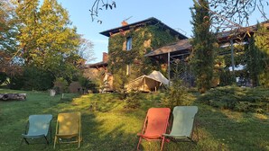 Een huis met een muur begroeid met klimop en een tuin met een houten terras en stoelen.