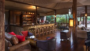Area esterna con un bar, arredi in legno, un bancone bar e un’area salotto con divani e poltrone in pelle.
