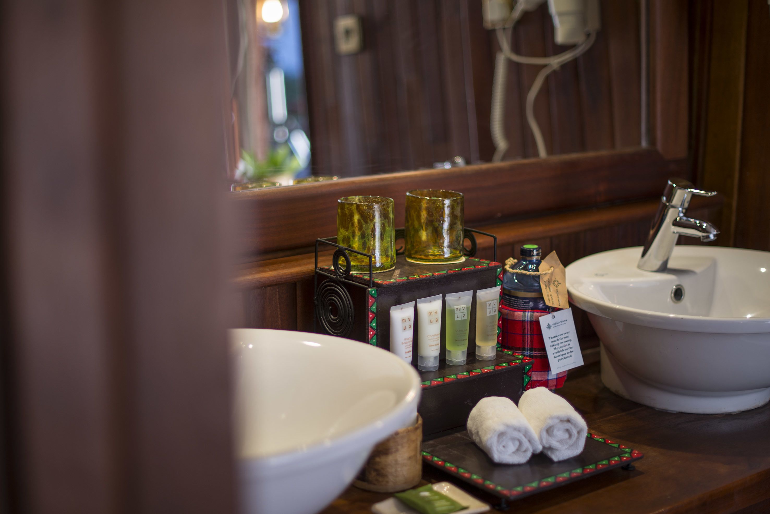 A bathroom with a large white basin, a sink, and a mirror. There are toiletries on a shelf, including bottles and a towel.