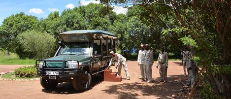 A safari vehicle parked on a dirt road with people standing nearby.