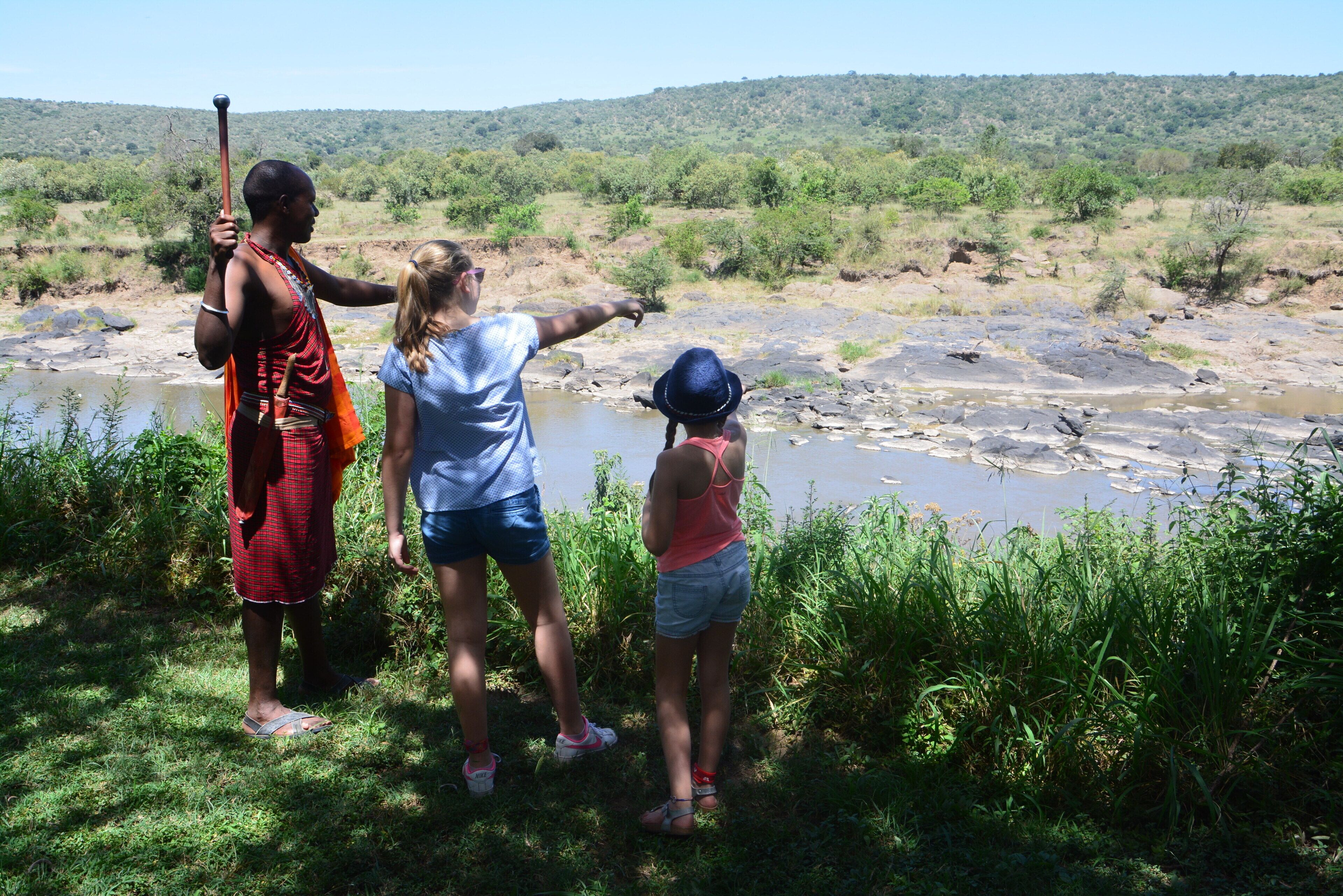 A group of people standing by a river with a natural landscape in the background.