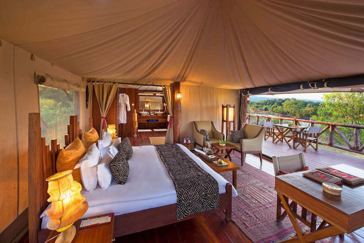A tented accommodation with a bed, seating area, and a view of the outdoors.
