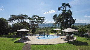 Una piscina con lettini e ombrelloni, circondata da erba e alberi, con vista su delle colline sullo sfondo.