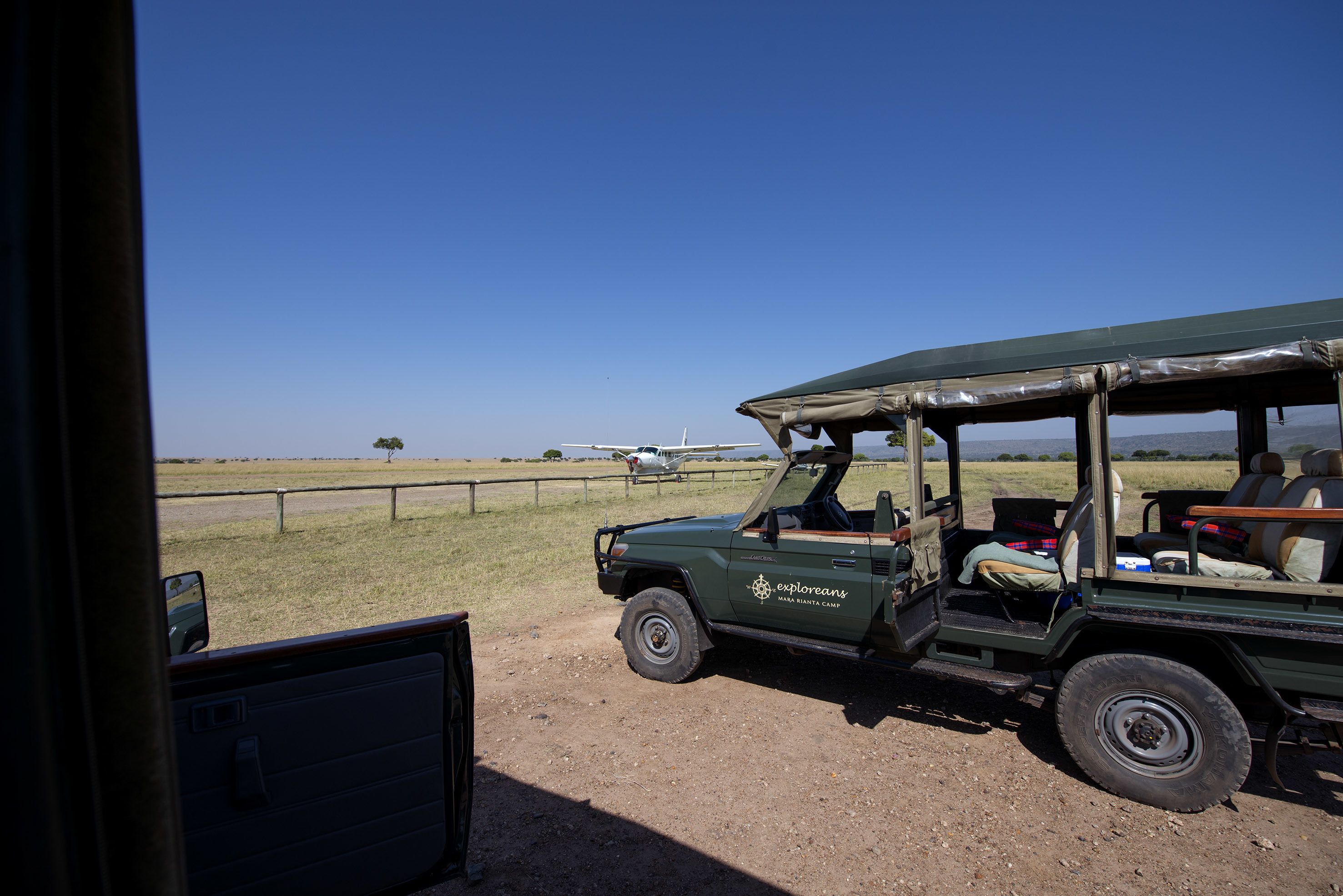 Un vehículo safari con capota, un pequeño avión al fondo y un campo cubierto de hierba.