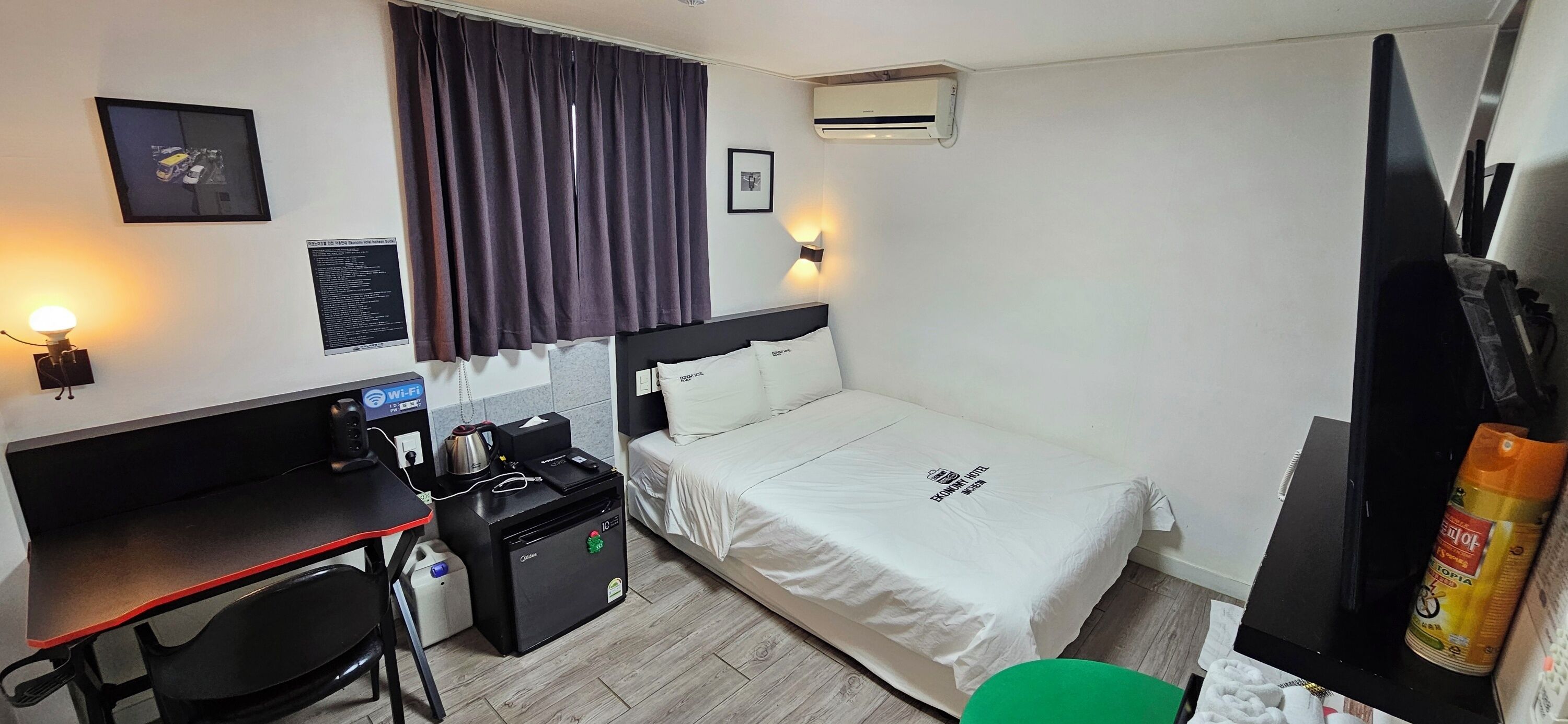 Habitación de hotel compacta con cama, escritorio, silla y una pequeña kitchenette.