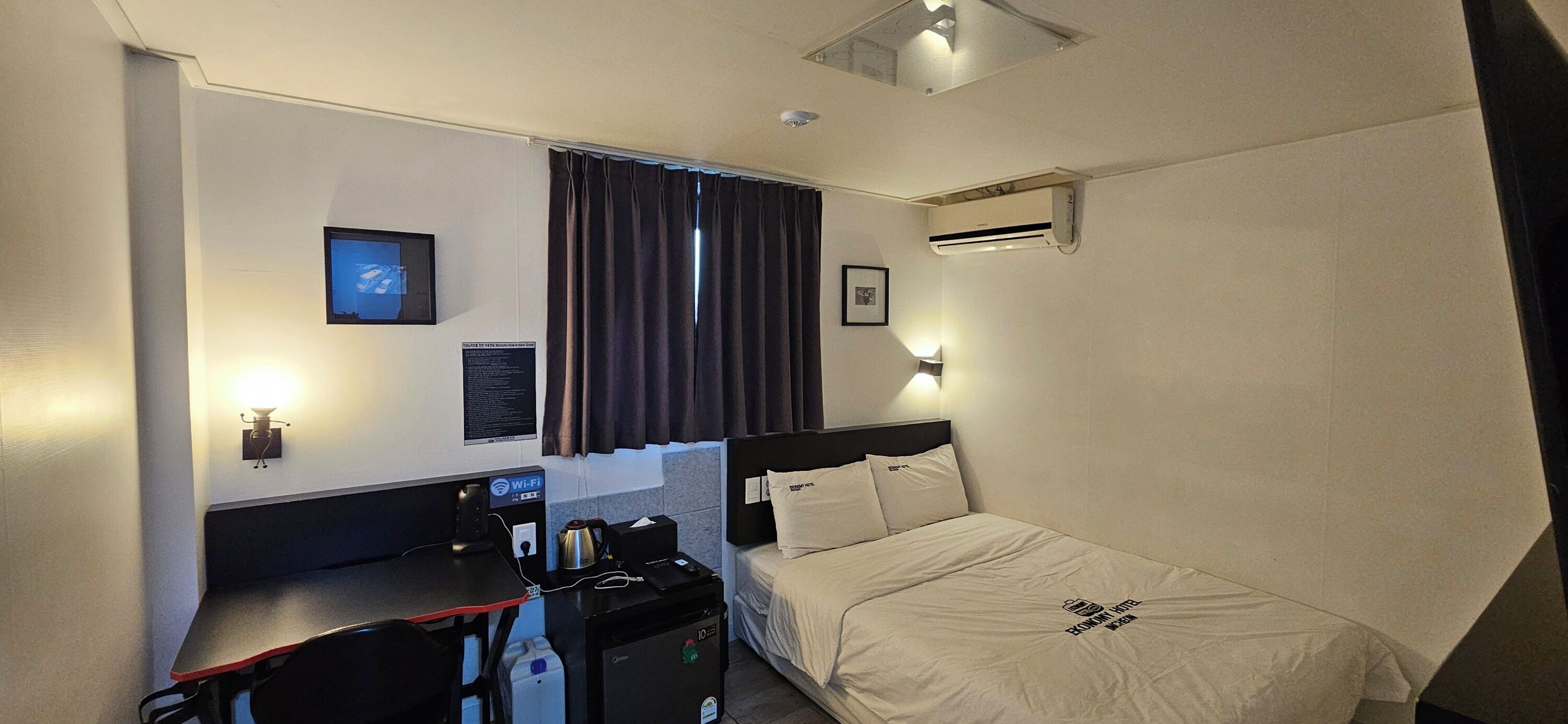 Une chambre d’hôtel équipée d’un lit, d’un bureau et d’une chaise, d’un téléviseur à écran plat, d’un climatiseur et d’un panneau indiquant la présence d’une connexion Wi-Fi.