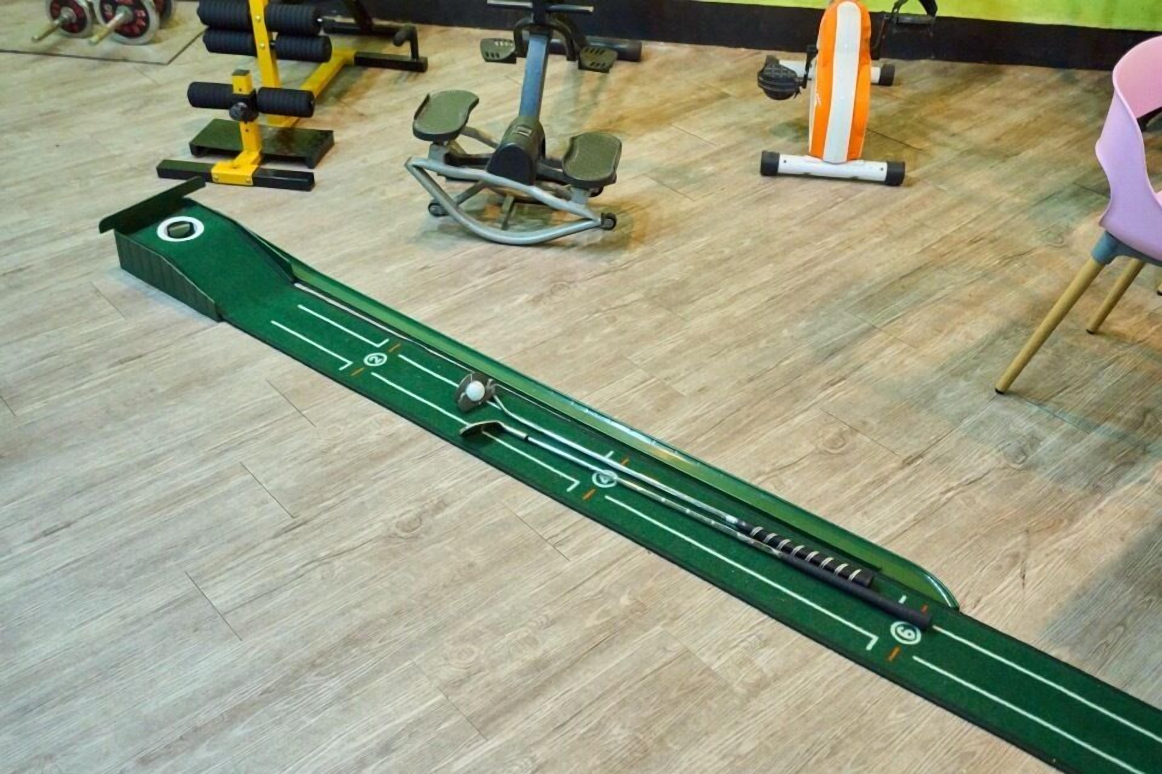 A green exercise machine on a wooden floor with gym equipment in the background.