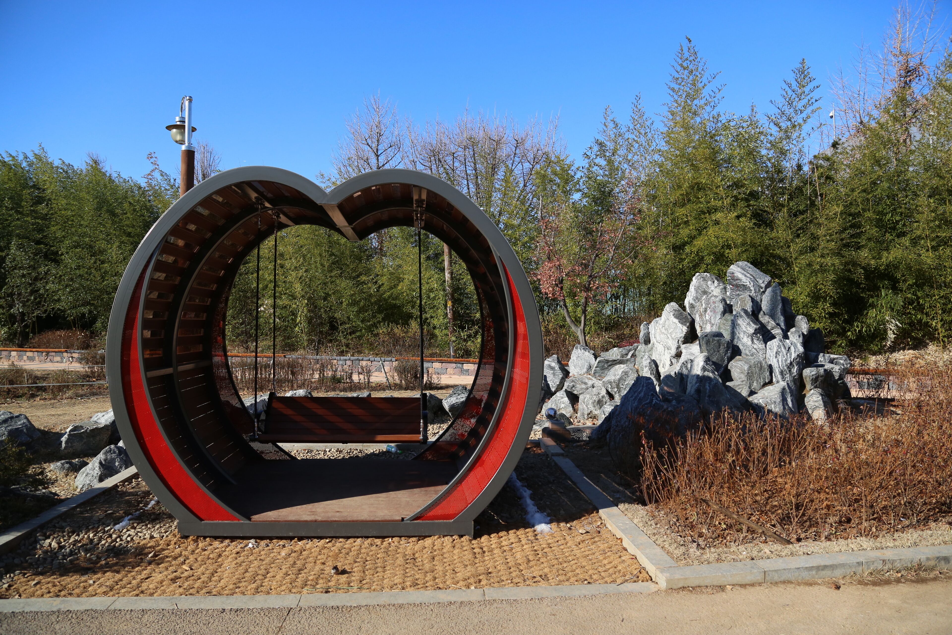 Una estructura con forma de corazón que alberga un banco, rodeada de rocas y árboles.