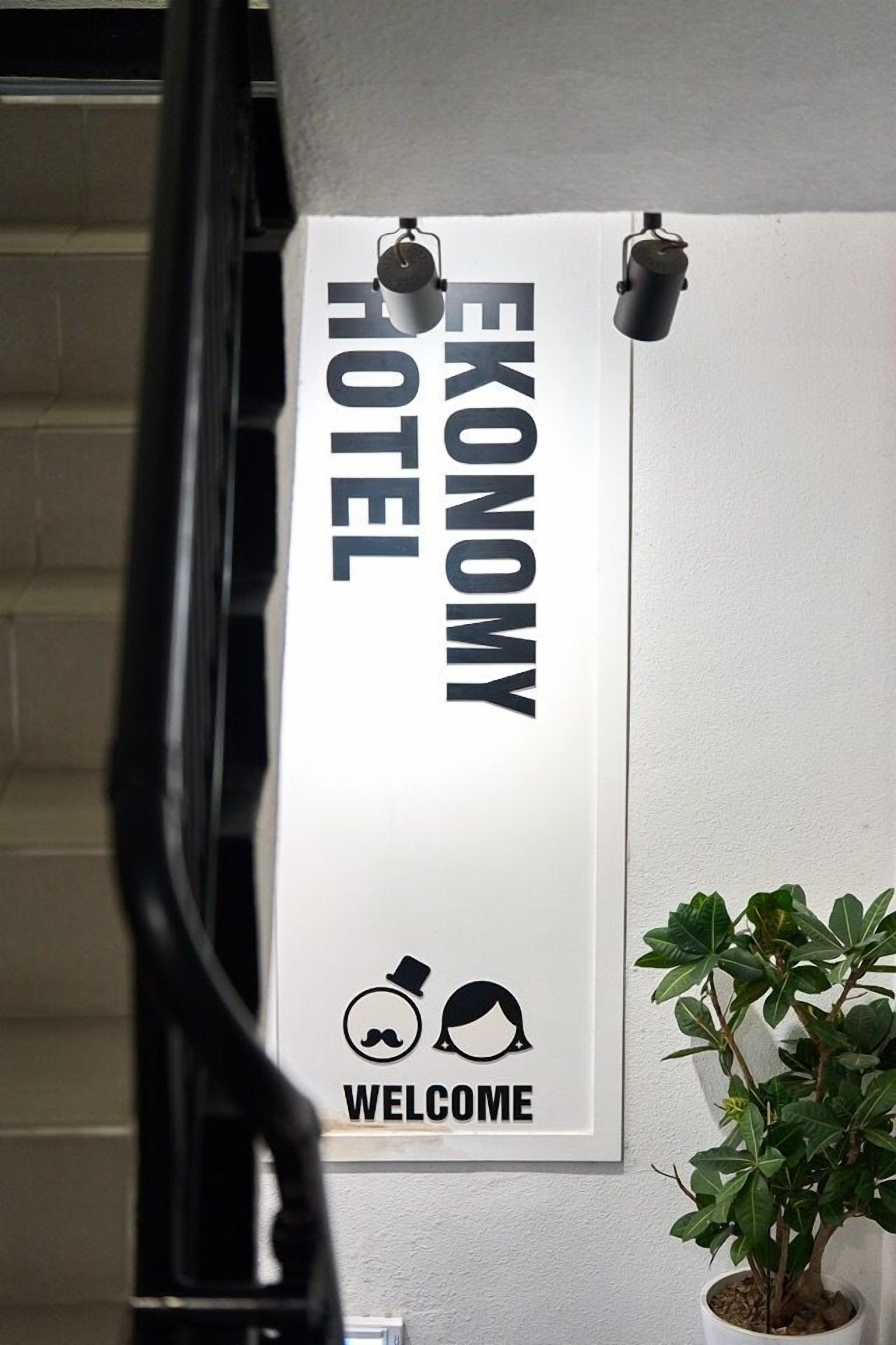 A sign with 'EKONOMY HOTEL' and a 'WELCOME' graphic with a mustache and hat.