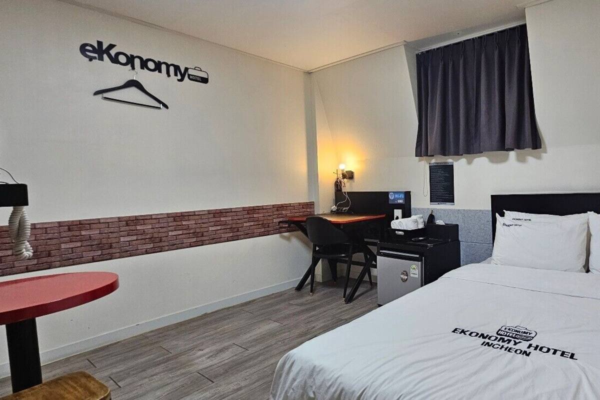 Une chambre d’hôtel équipée d’un lit, d’un bureau, d’une chaise, d’une petite table et d’un téléviseur fixé au mur.