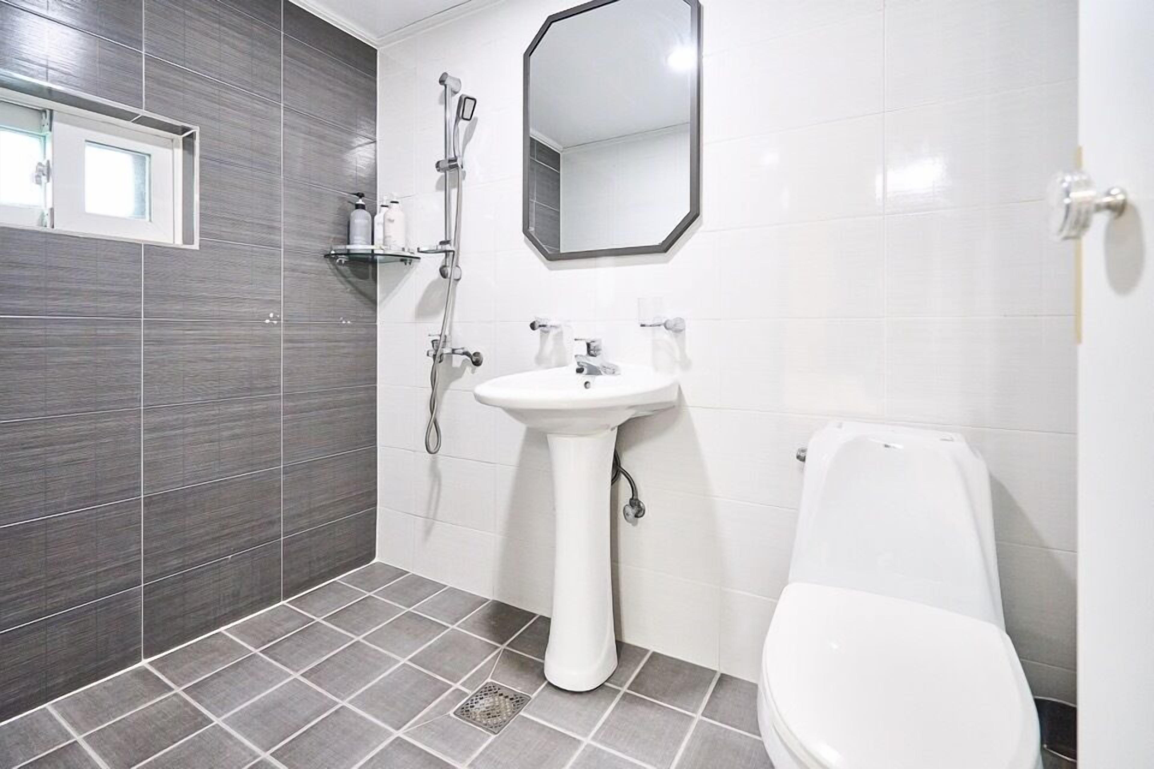 Un baño con lavamanos pedestal, inodoro, ducha y espejo.