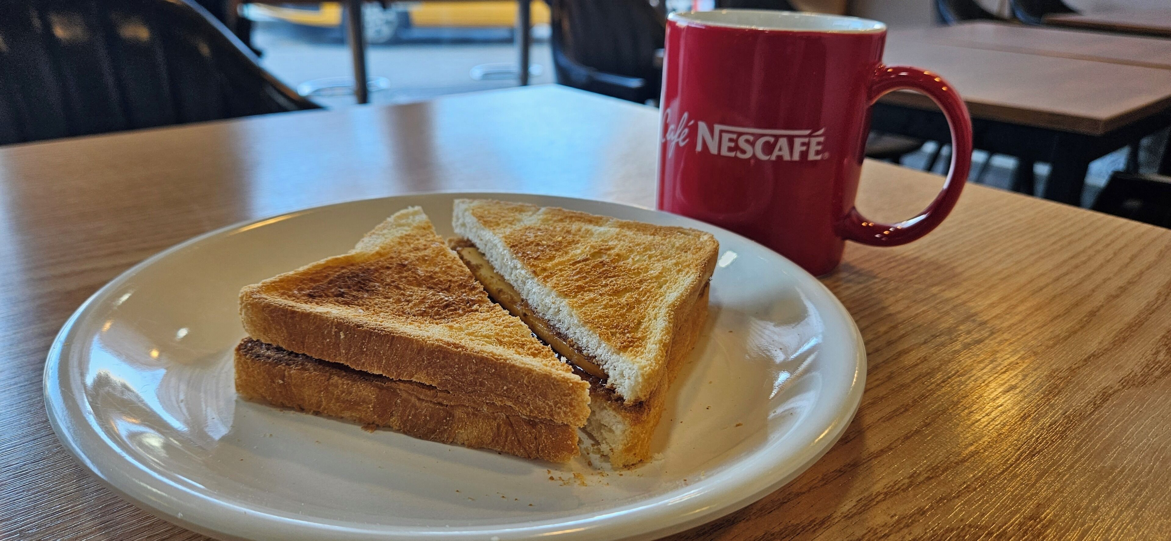 Une assiette avec un sandwich et une tasse rouge sur une table en bois.