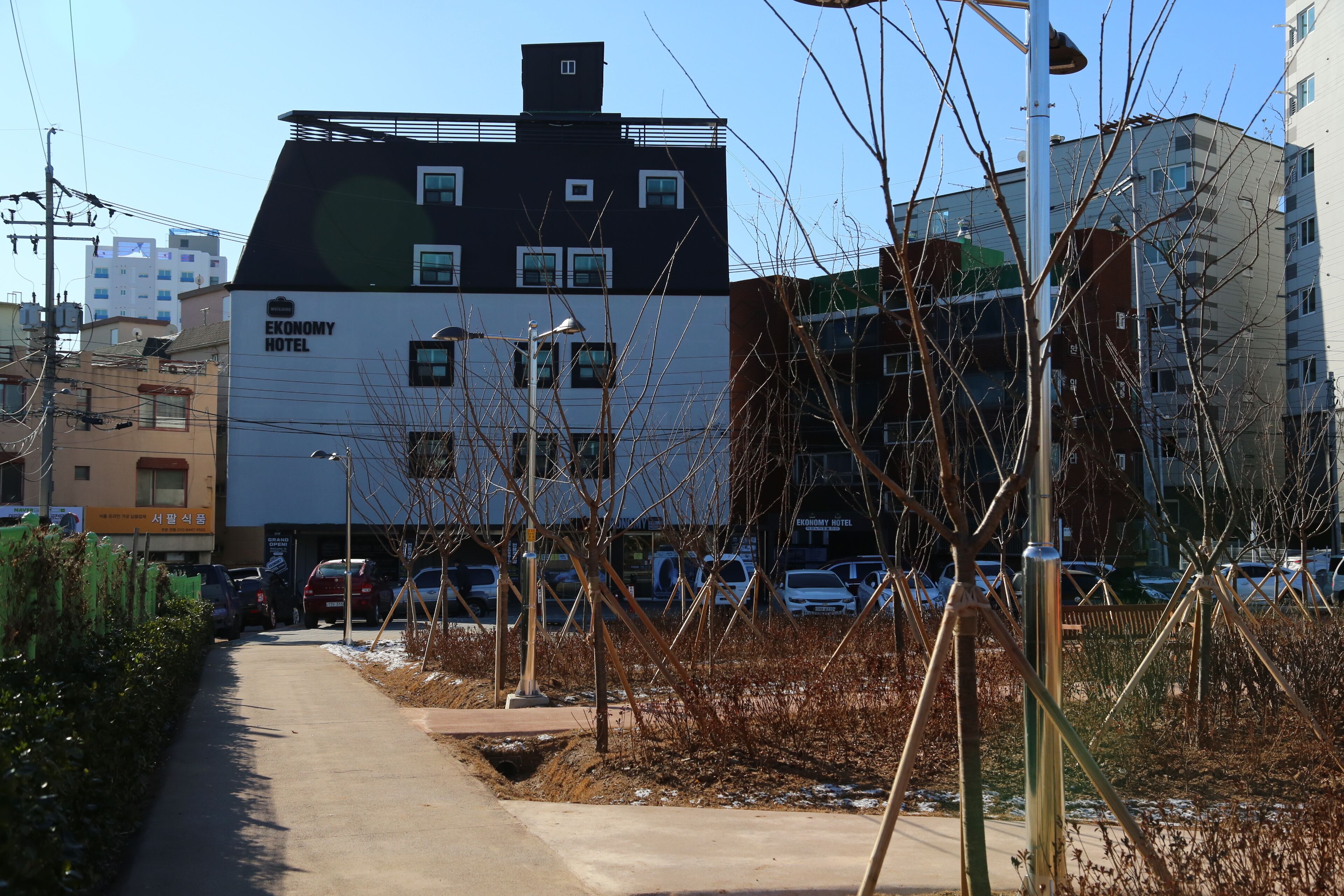 A building with a sign reading 'Economy Hotel,' surrounded by parked cars and a sidewalk.