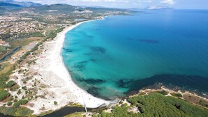 Oversigtsbillede af et kystområde med en strand, klart blåt vand og et bjergrigt baggrundsmotiv.