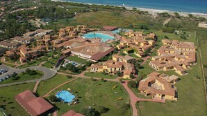 Oversigtsbillede af en kystresort med flere bygninger, en central swimmingpool og en strand i baggrunden.