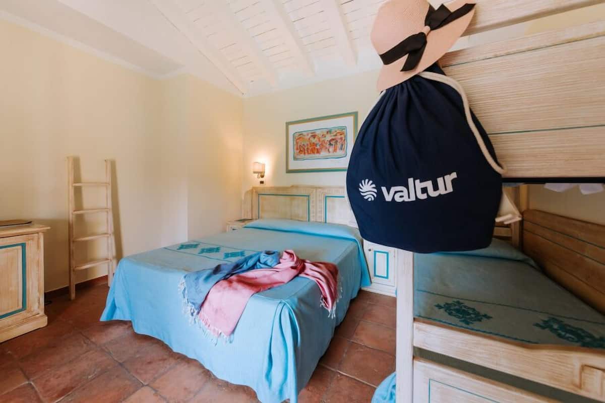 A room with two beds, a wooden wardrobe, a ladder, and a wall-mounted bag with 'vallur' logo.