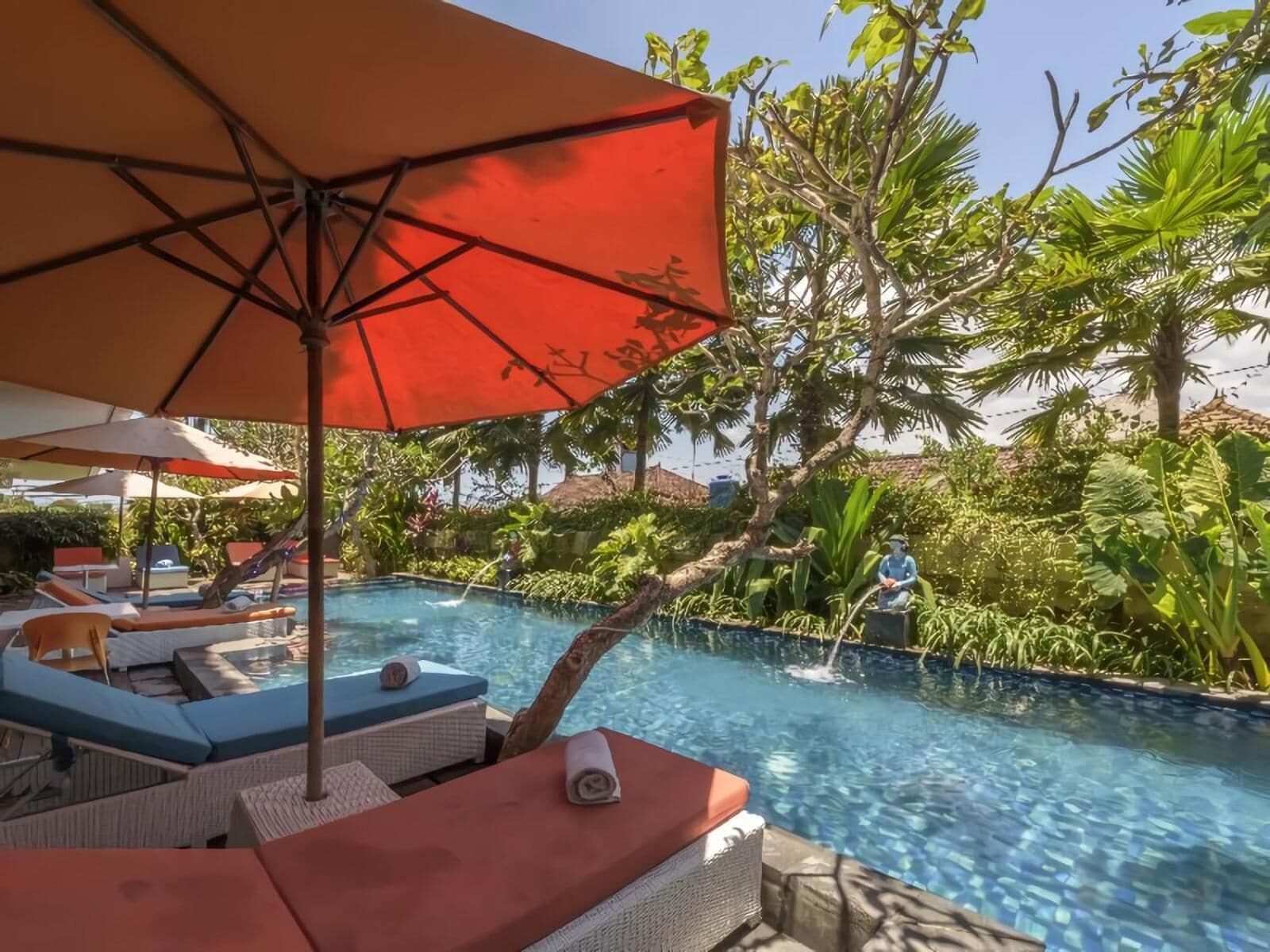 Un espace piscine agrémenté de chaises longues et de parasols, entouré d’une végétation luxuriante.
