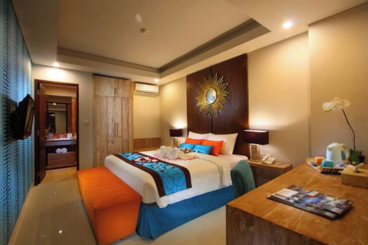 Quarto de hotel com cama grande, mesas de cabeceira, escrivaninha e espelho.