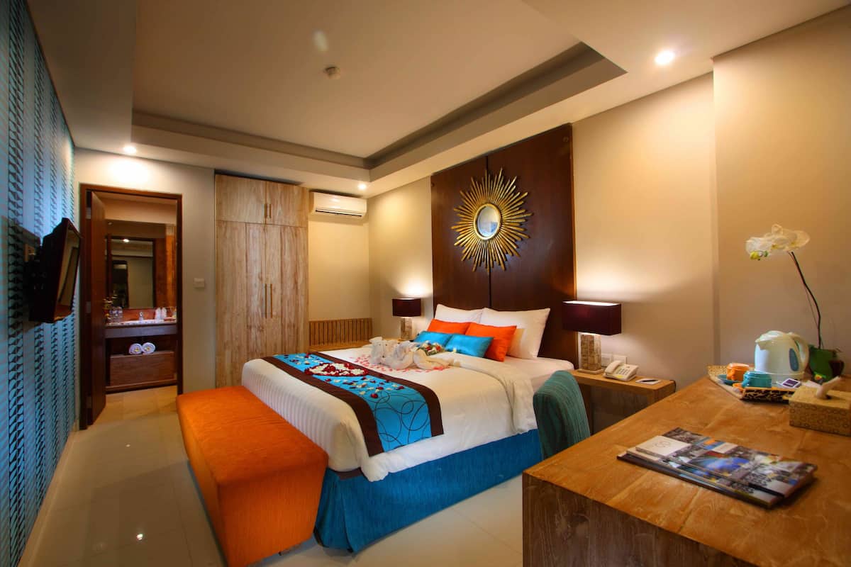 Ein Hotelzimmer mit einem großen Bett, einem Holzkopfende, einem Nachttisch, einem Schreibtisch und einem Spiegel an der Wand.