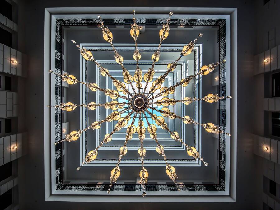 A grand chandelier with multiple arms and light fixtures, centered in a square frame with a mirrored ceiling.