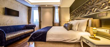 A modern hotel room with a large bed, a sofa, a flat-screen TV mounted on the wall, and a decorative headboard.