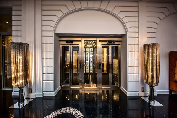Entrada de ascensor con diseño moderno, dos grandes columnas decorativas y un piso negro pulido.