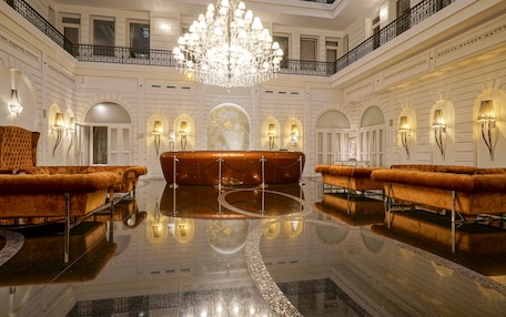A luxurious lobby with a grand chandelier, plush seating, and elegant wall sconces.