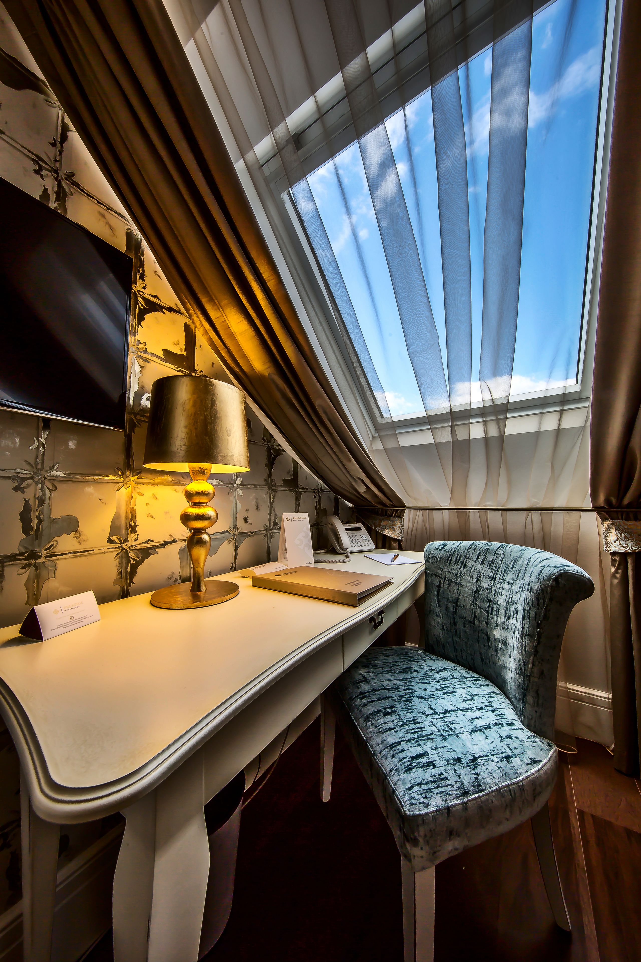A room with a desk, a chair, a lamp, a TV, and a skylight.
