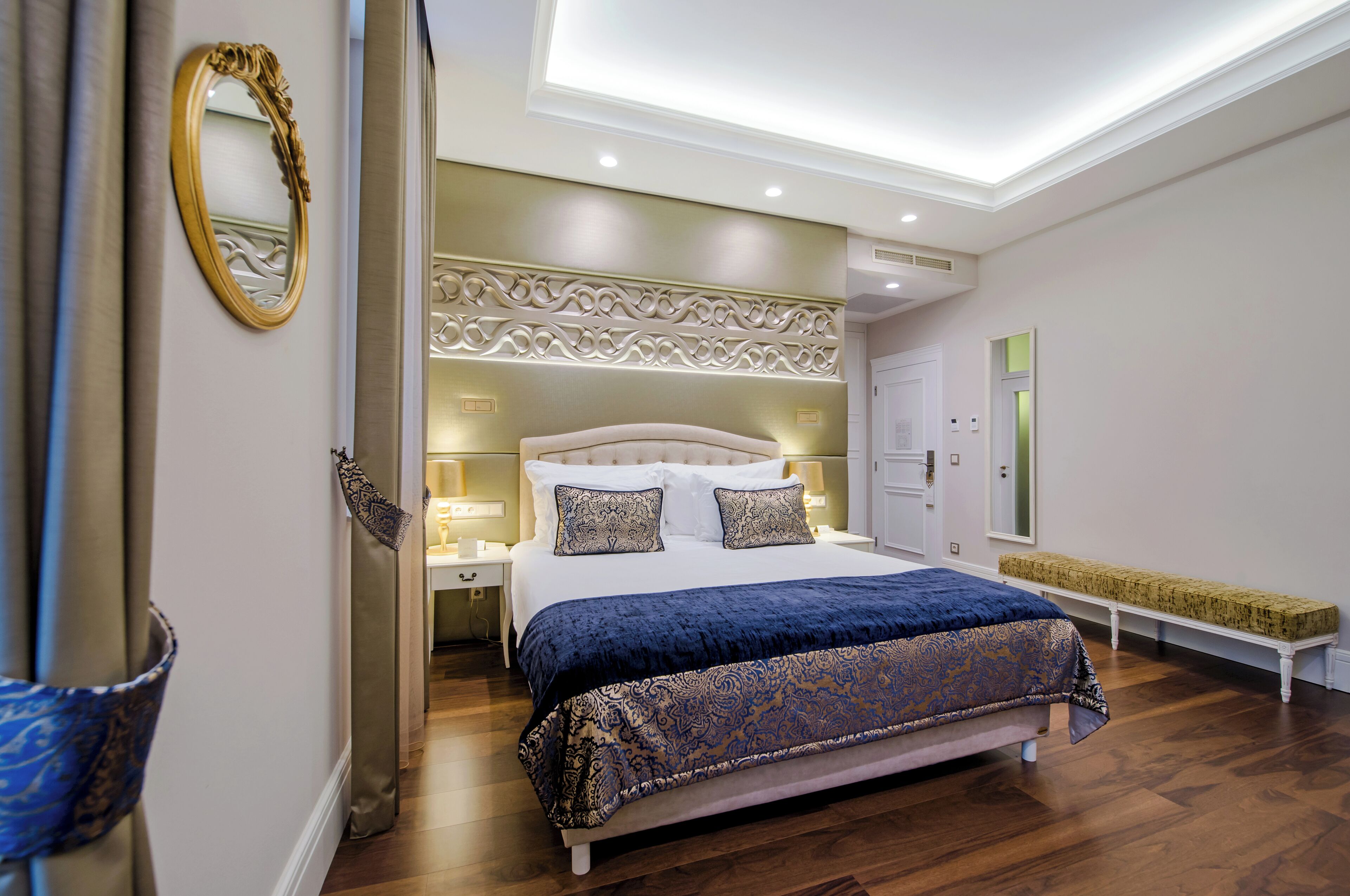 Un dormitorio con una cama grande, mesitas de noche, un banco y un espejo.