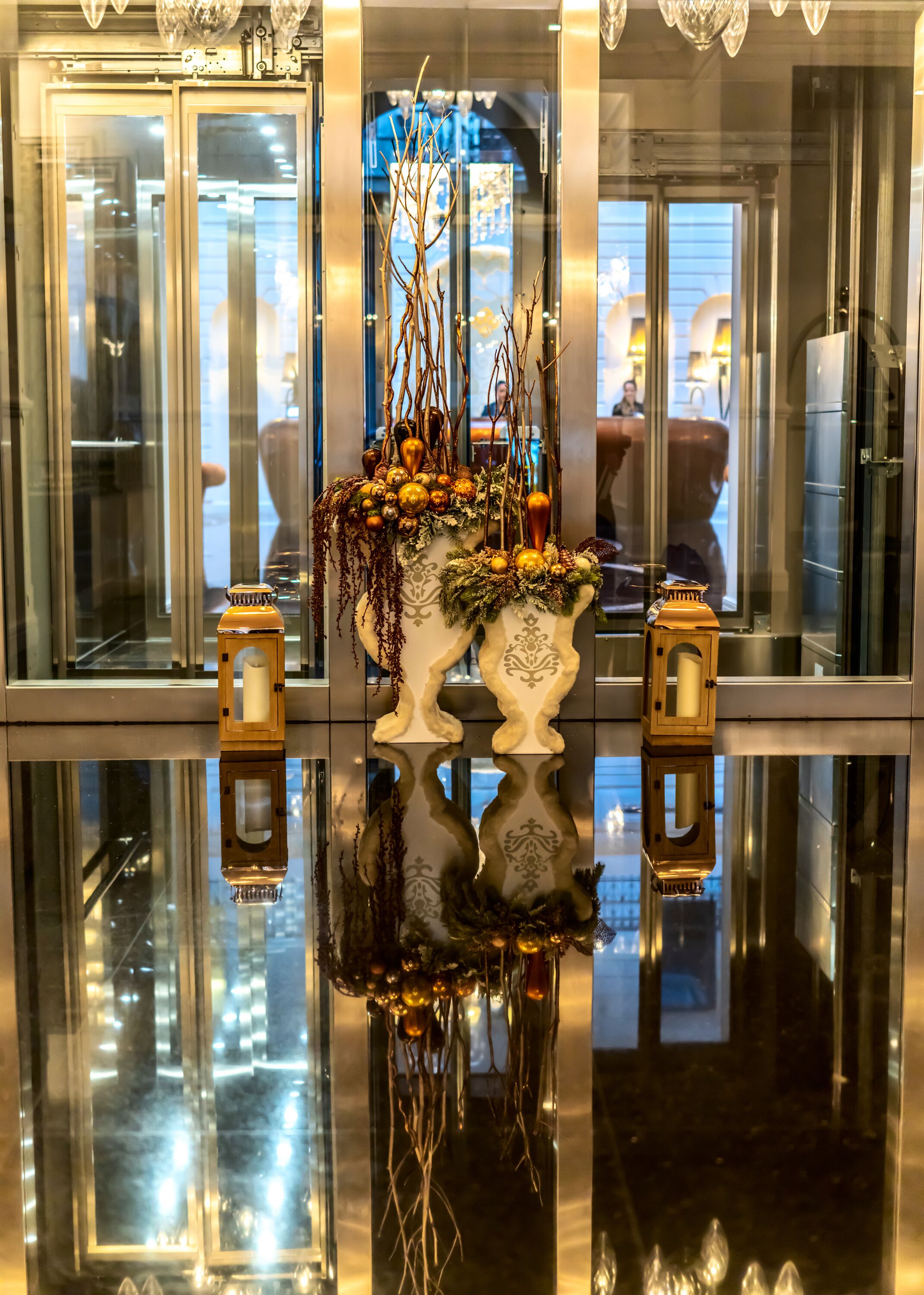 A reflective glass table with two ornate vases containing decorative branches and ornaments.