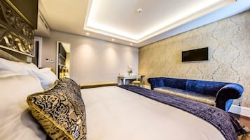 Ein Hotelzimmer mit einem großen Bett, einem blauen Sofa, einem kleinen Tisch und einem an der Wand befestigten Fernseher.