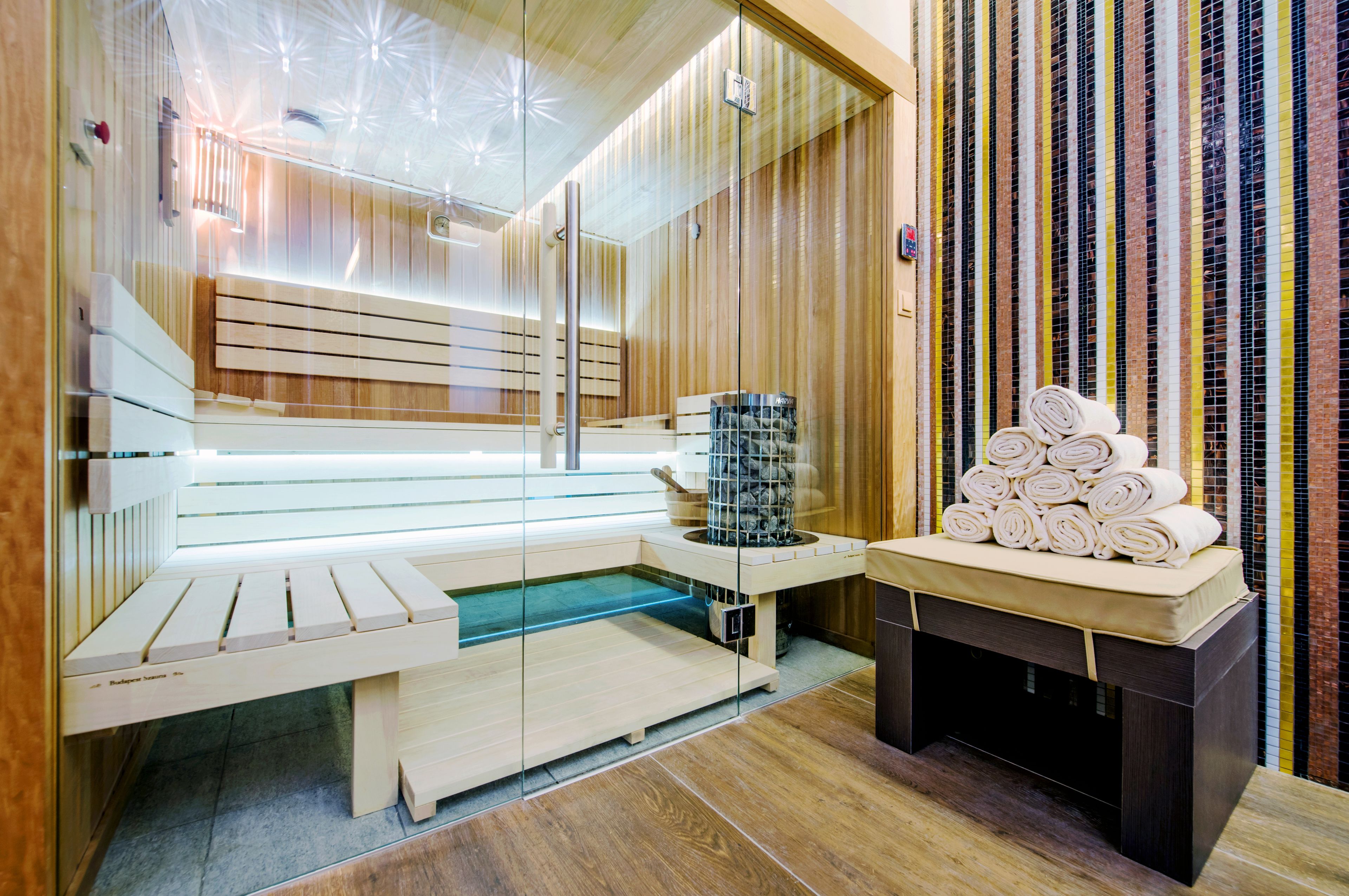 Un sauna avec des bancs en bois, un banc entouré de parois en verre et une pile de serviettes.
