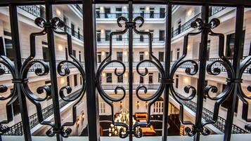 Vista a través de elaboradas rejas de hierro de un edificio de varios pisos con balcones y una araña central.