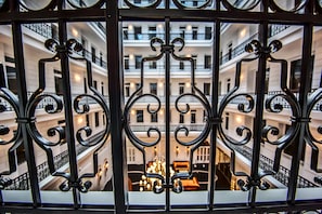 A view through ornate iron gates of a multi-story building with balconies and a central chandelier. - Prestige Hotel Budapest (Budapest)