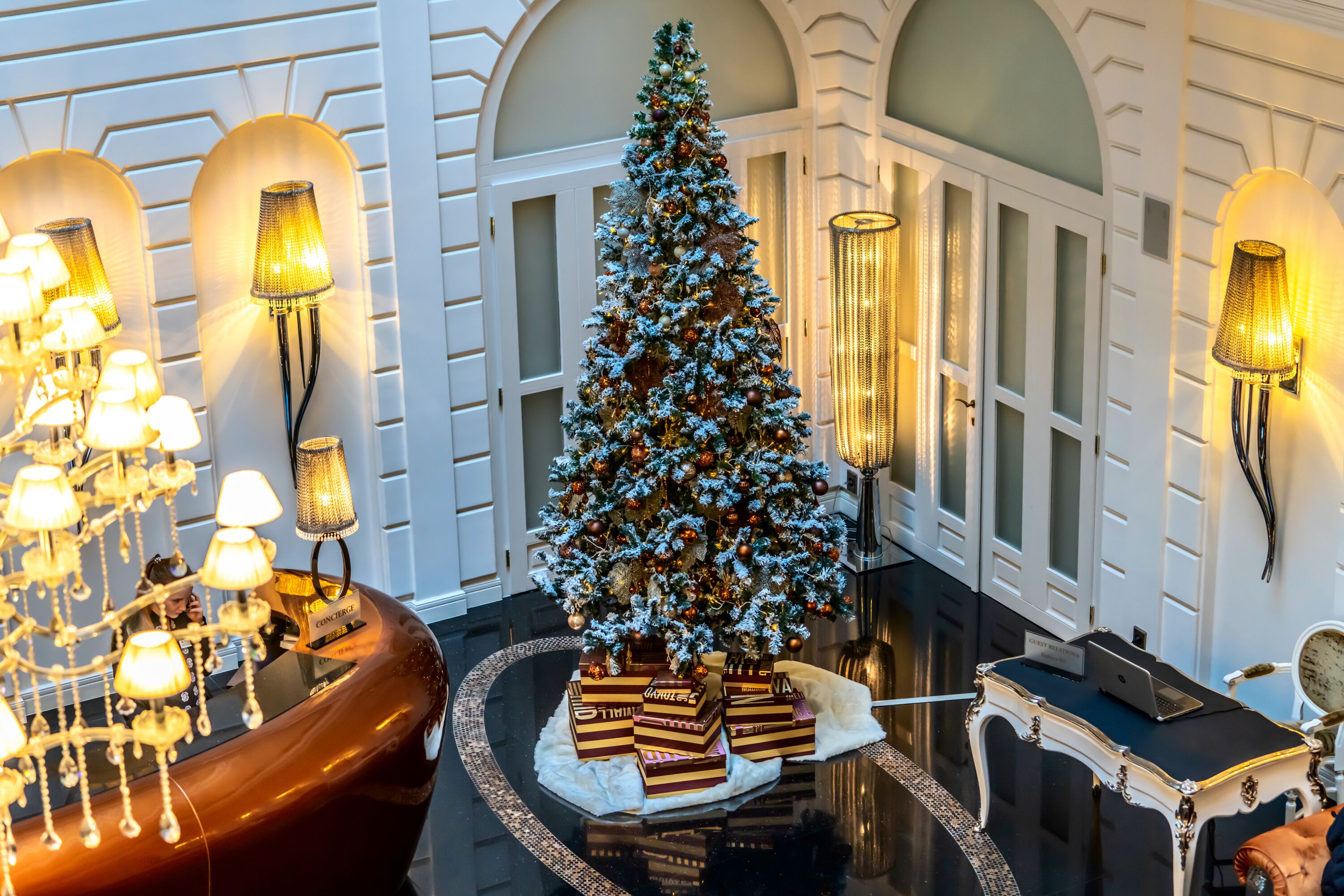 Un vaste hall d’entrée agrémenté d’un grand sapin de Noël, de lustres élégants et d’un luxueux comptoir de réception.