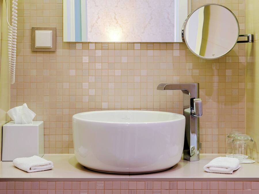Un baño con un lavamanos grande de color blanco, un espejo, un dispensador de toallas y un teléfono.