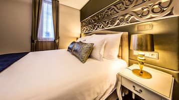 A neatly made bed with white linens and a decorative pillow, a bedside table with a lamp, and a wall with an ornate design.