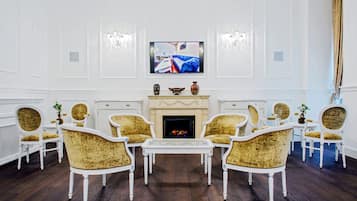 Una habitación con chimenea, muebles blancos y un televisor montado encima.