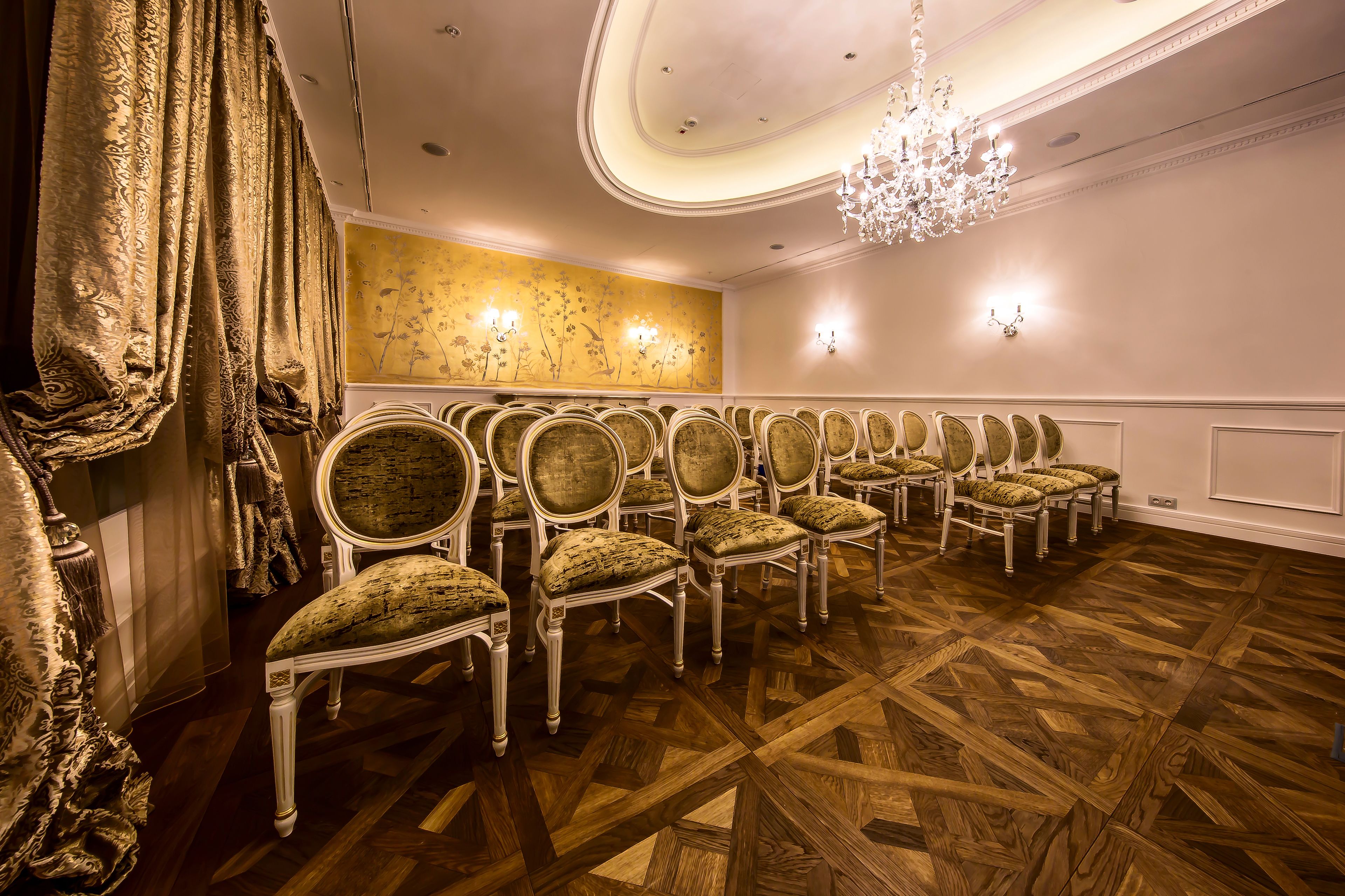 A room with a row of upholstered chairs, a patterned carpet, and a chandelier.